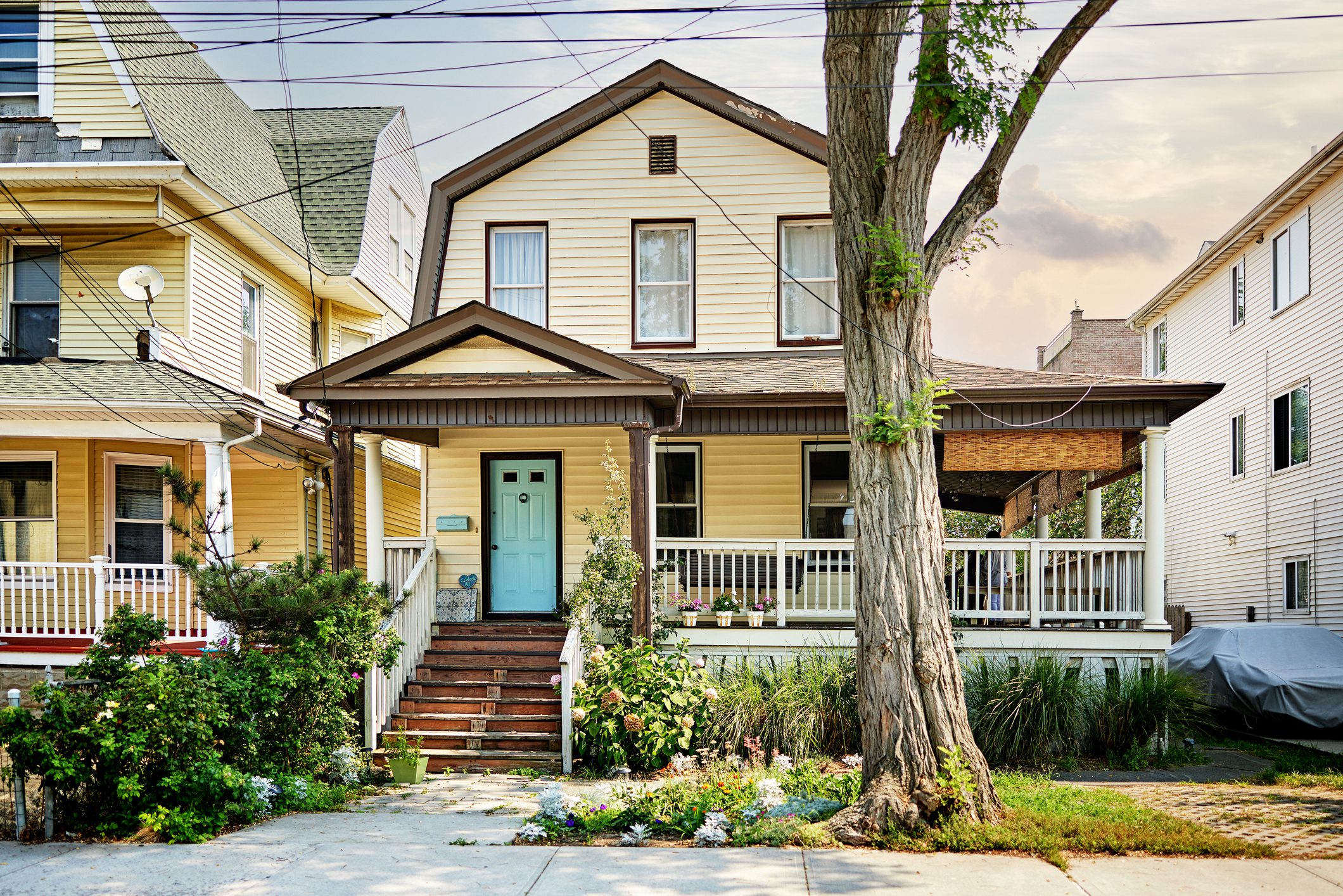 Yellow house with porch and tree outside.